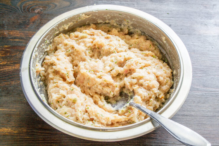 Adding melted butter to the ground chicken for extra richness and moisture. Melted butter being poured into a bowl of ground chicken mixture.