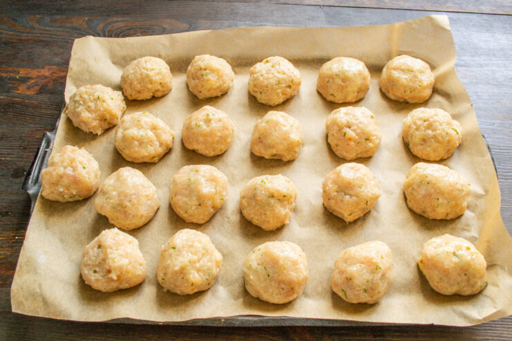 Shaping the ground chicken mixture into perfectly round tefteli. Hands shaping the ground chicken mixture into small, uniform meatballs (tefteli).