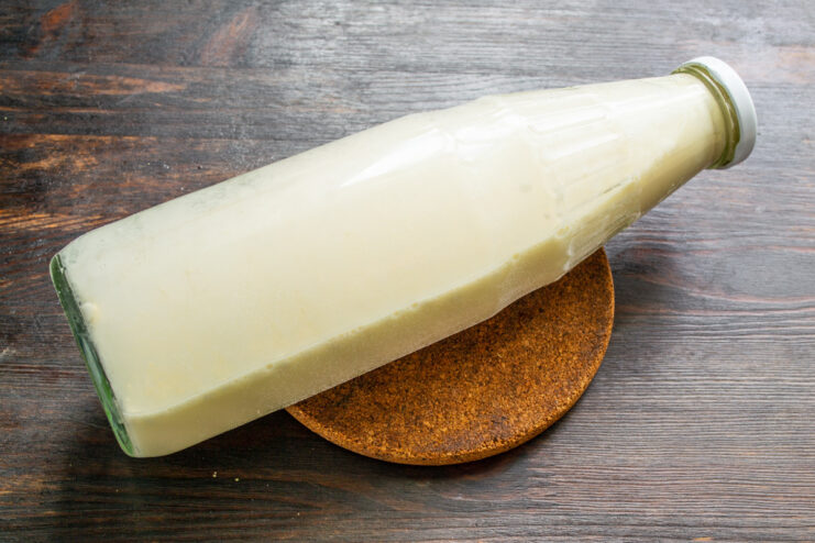 The secret to lump-free batter: just shake the bottle! A hand shaking a sealed plastic bottle to mix the pancake batter inside.