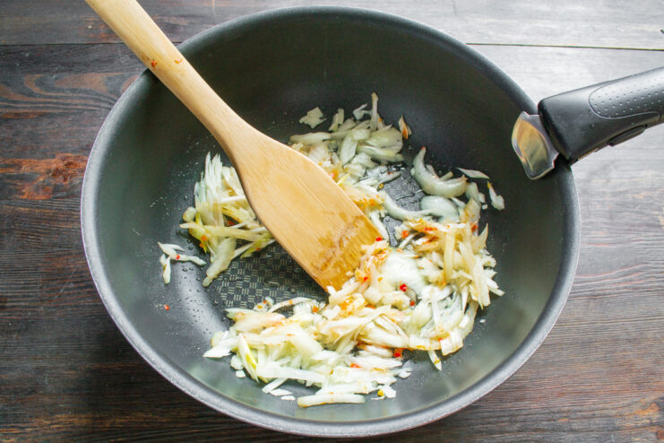 Sautéing Onions and Garlic for a Flavorful Base Sliced onions being added to a skillet with garlic and spices to create a flavor base.