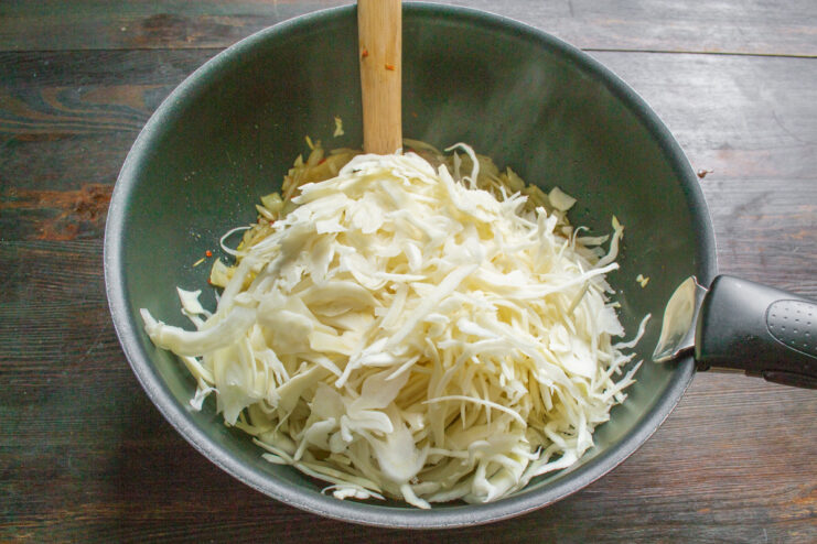 Adding Shredded Cabbage to the Skillet A large amount of shredded white cabbage being added to the skillet with sautéed onions.