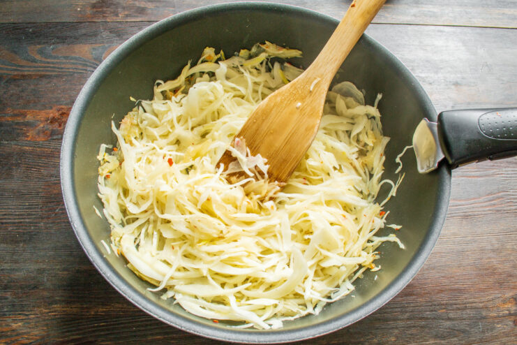 Tossing Cabbage and Onions Over High Heat Shredded cabbage being mixed with sautéed onions in a large skillet over the stove.