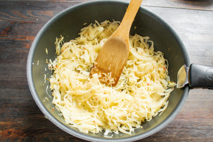 Deglazing the Pan with White Wine for Extra Flavor Dry white wine being poured into a skillet with cabbage and onions.