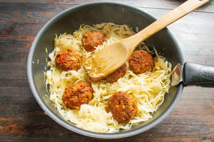 Adding Pan-Fried Meatballs Back to the Cabbage Golden-brown pan-fried meatballs being placed on top of the braised cabbage in the skillet.