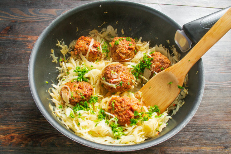 Finishing the Dish with Fresh Parsley Freshly chopped parsley being sprinkled over the braised cabbage and meatballs in the skillet.