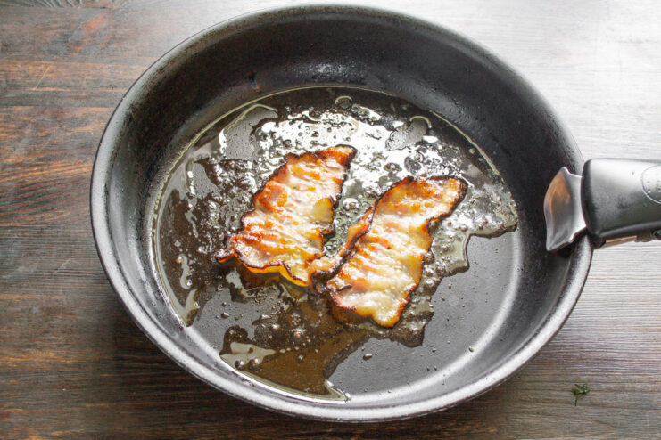 Frying Bacon Until Crispy for the Garnish Strips of smoked bacon frying in a hot skillet.