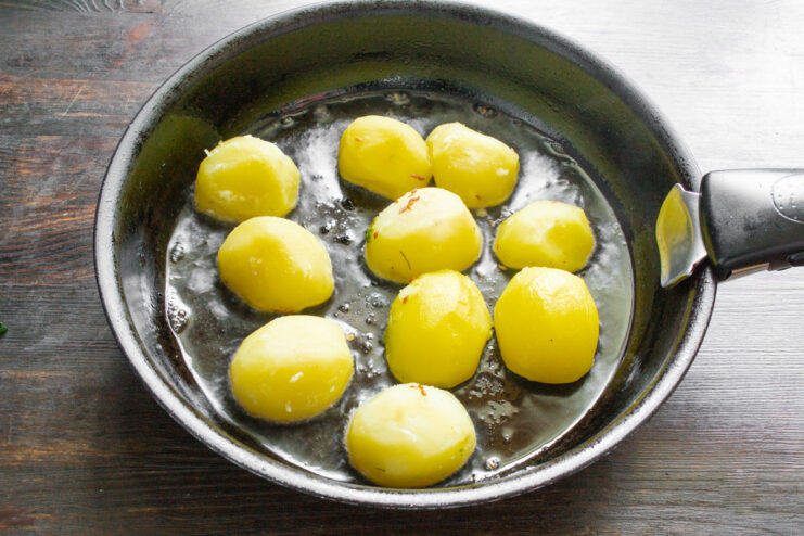 Adding Boiled Potatoes to the Skillet to Fry Boiled potato halves being placed cut-side down into a hot skillet with oil.