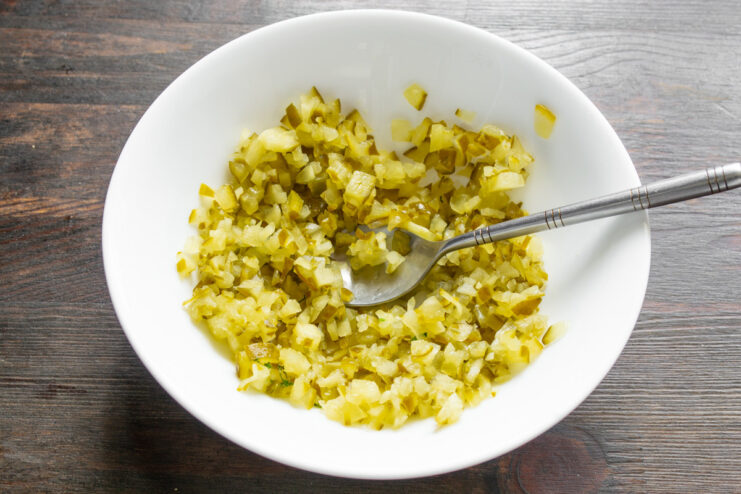 Preparing the Pickle for the Creamy Sauce A hand dicing a salted pickle into small cubes on a cutting board.