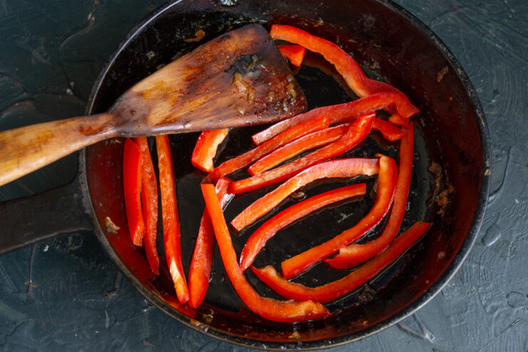 Sautéing Red Bell Pepper Strips in a Pan Thin strips of red bell pepper being sautéed in a hot frying pan.