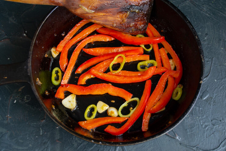Adding Garlic and Chili for an Aromatic Base Sliced garlic and chili pepper rings added to the sautéed bell peppers in a pan.