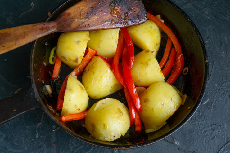 Combining Boiled Potatoes with Peppers and Olive Oil Boiled new potatoes being added to the pan with peppers, drizzled with olive oil.