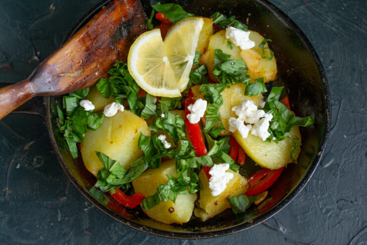 Adding a Zesty Finish with Fresh Lemon Juice Squeezing fresh lemon juice over the Greek-style potatoes in the pan.