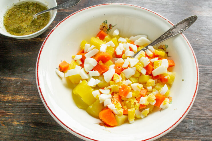 Adding Chopped Hard-Boiled Eggs for Extra Richness Finely chopped hard-boiled eggs being added to the bowl with potatoes and carrots.