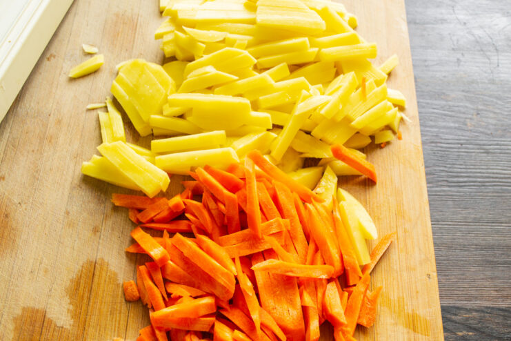 Slicing Potatoes and Carrots into Batons for Frying Close-up of peeled potatoes and carrots being sliced into uniform batons on a cutting board.