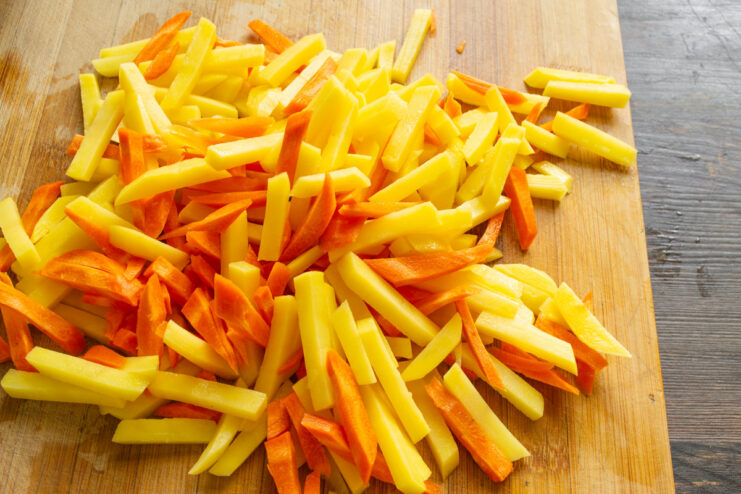 Combining Sliced Potatoes and Carrots Before Frying A bowl containing a mix of sliced raw potato and carrot batons, ready for cooking.