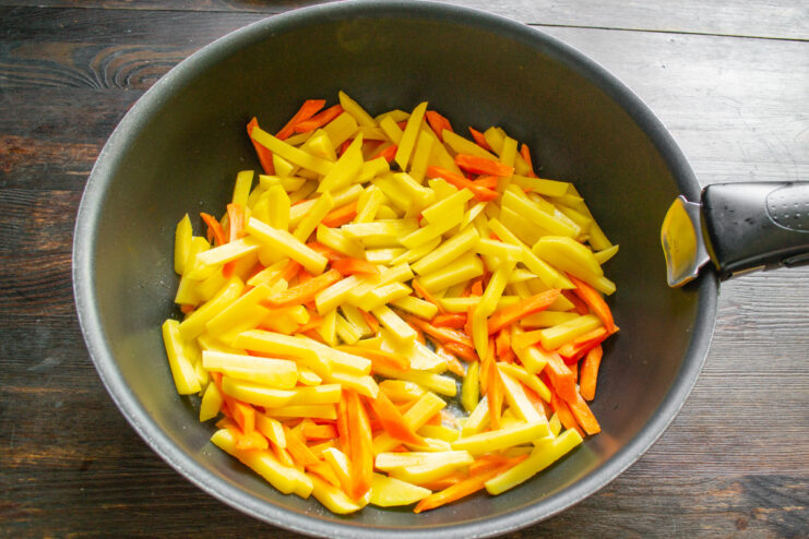 Adding Potatoes and Carrots to a Hot Pan with Oil Sliced potatoes and carrots being added to a hot skillet with sizzling oil.