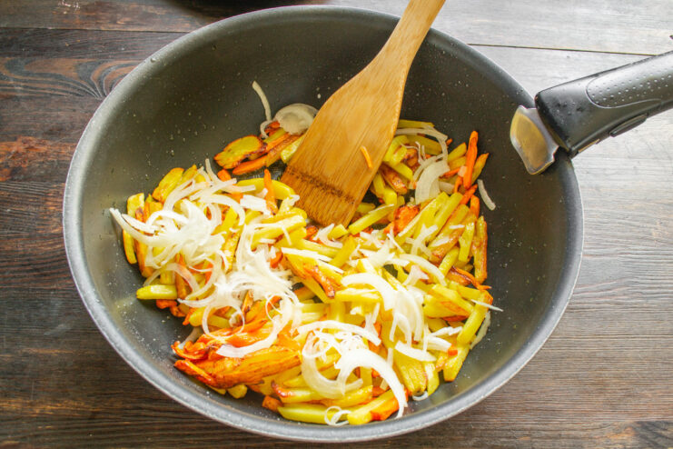 Adding Onions and Salt to the Pan-Fried Potatoes Sliced onions and coarse sea salt being added to the pan of partially cooked potatoes and carrots.