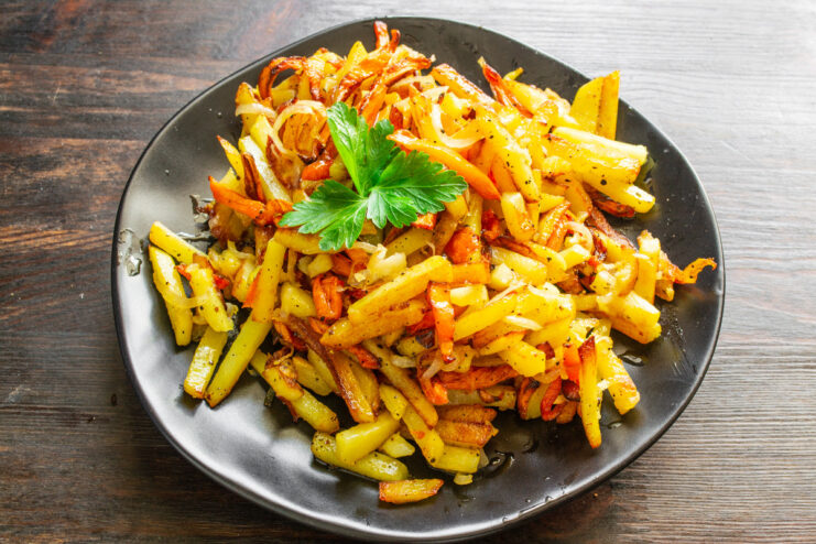 Garnishing the Fried Potatoes with Pepper and Parsley Before Serving A serving of hot fried potatoes with carrots and onions, garnished with fresh parsley and black pepper.
