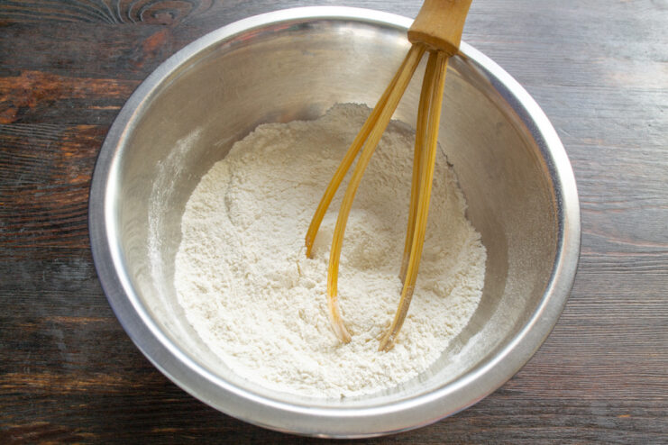 Step 1: Combining the dry ingredients for the cake batter. A white bowl with flour and baking powder being mixed with a whisk.