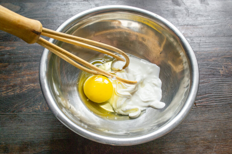 Step 1: Combining the wet ingredients for the muffin batter A white bowl containing sour cream and a cracked egg, ready to be mixed.