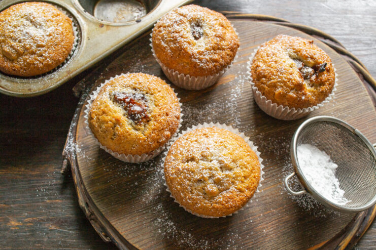 The final touch: dusting warm muffins with powdered sugar Freshly baked walnut and date muffins being dusted with powdered sugar.
