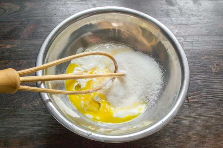 Adding sugar to the wet ingredients Granulated sugar being poured into the bowl with sour cream and egg.