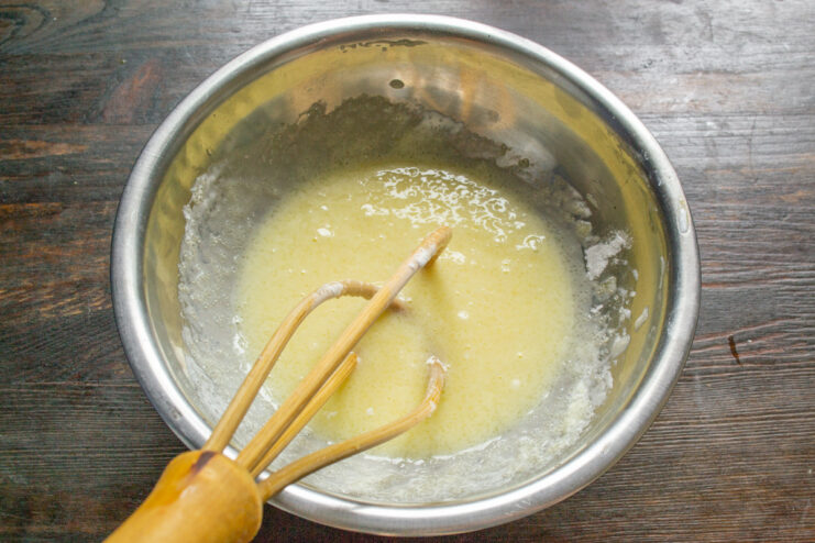 Whisking the batter until smooth and creamy A hand whisking egg, sour cream, and sugar in a white bowl.
