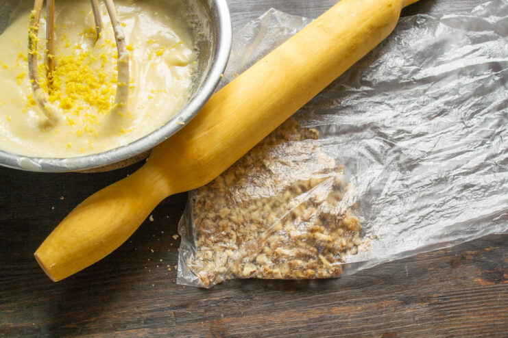 Crushing walnuts to add to the muffin batter Crushing walnuts inside a plastic bag with a wooden rolling pin.