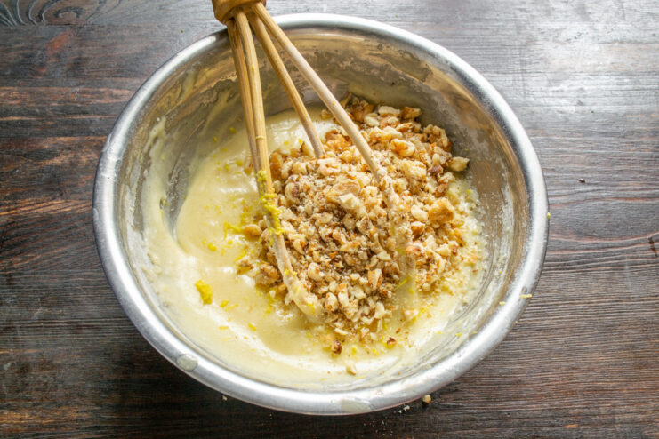 Folding crushed walnuts into the muffin batter Muffin batter in a bowl with crushed walnuts being mixed in.