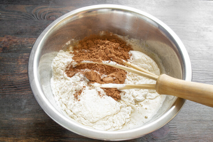 Step 3: Adding dry ingredients to the wet mixture Sifted flour and cocoa powder being added to the liquid batter in a bowl.