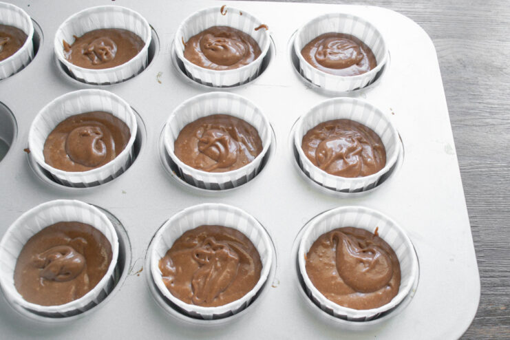 Step 6: Filling cupcake liners with batter before baking A muffin tin with paper liners being filled with chocolate batter.