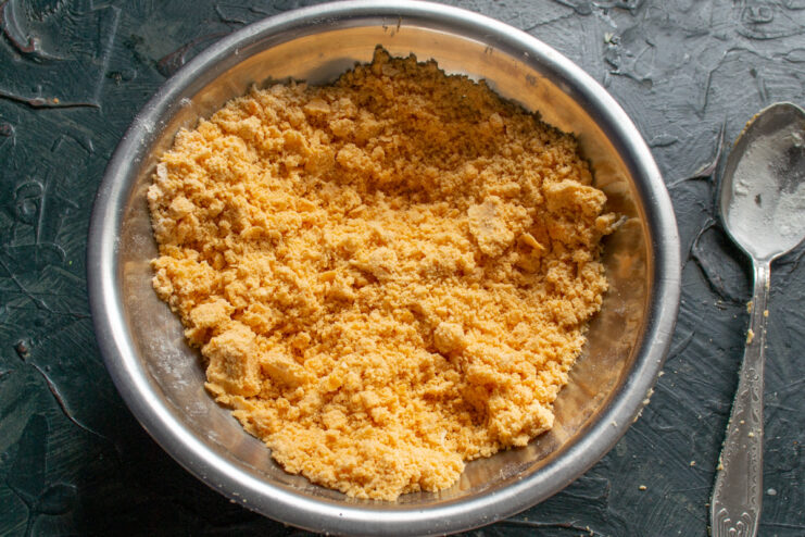 Creating a Crumbly Texture for the Dough Hands rubbing butter and flour together to create bright orange, cheesy breadcrumbs.