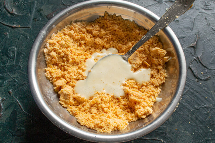 Adding Egg to Bind the Quiche Dough Adding the liquid egg mixture to the flour and butter crumbs in a bowl.
