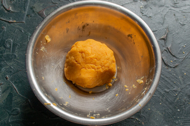 Chilling the Quiche Dough Before Rolling A ball of orange-colored quiche dough wrapped in plastic wrap, ready for chilling.