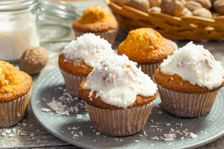 A plate of freshly baked coconut cupcakes, topped with white cream and a sprinkle of shredded coconut.
