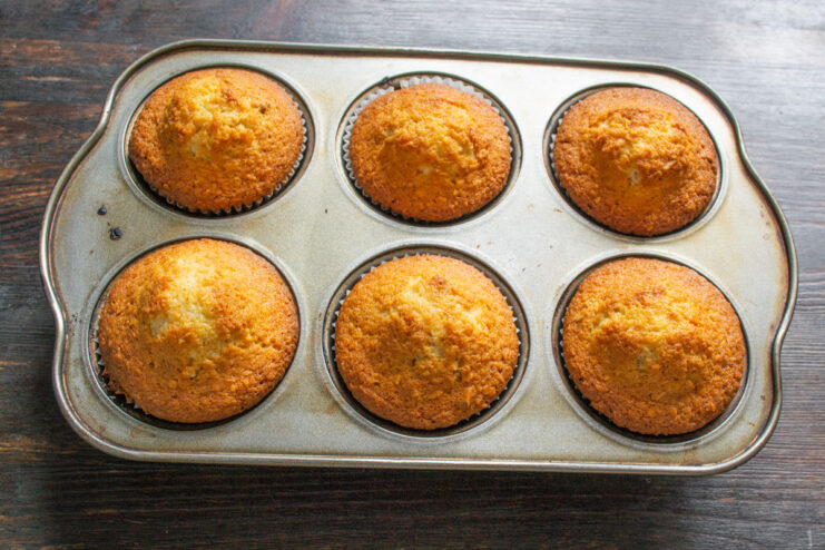 Freshly baked coconut cupcakes cooling on a rack Golden-brown coconut cupcakes cooling on a metal wire rack after baking.
