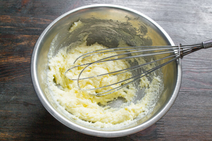The process of whipping butter, sugar, and vanilla until light and fluffy Close-up of a creamy butter and sugar mixture being whisked in a bowl.