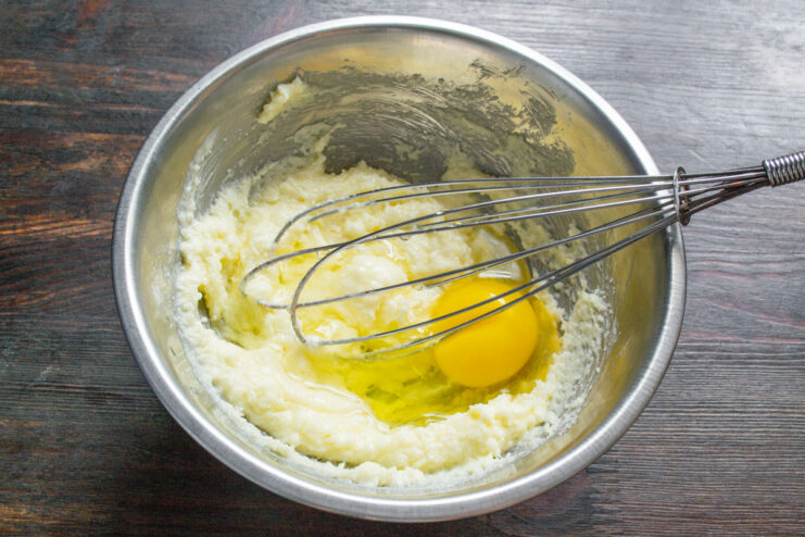 Adding an egg to the cupcake batter An egg being cracked into a bowl with the creamed butter and sugar mixture.