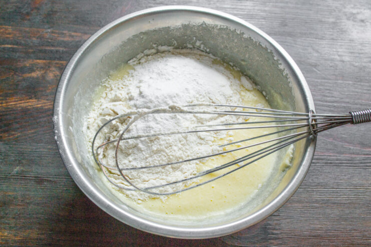 Adding dry ingredients to the wet mixture Sifting flour and baking powder into the cupcake batter.