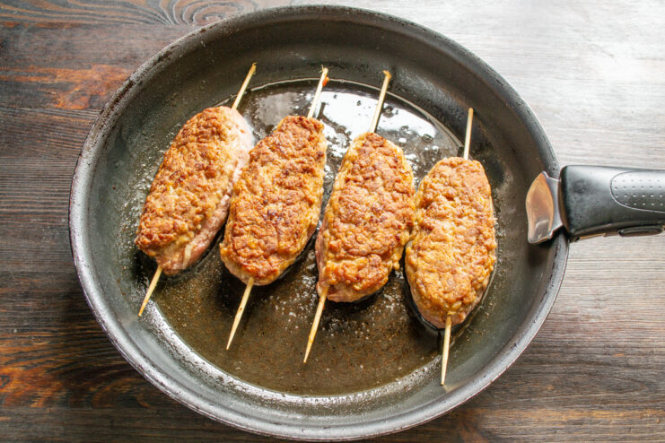 Pan-Frying the Beef Sausages Beef sausages on skewers browning in a skillet.