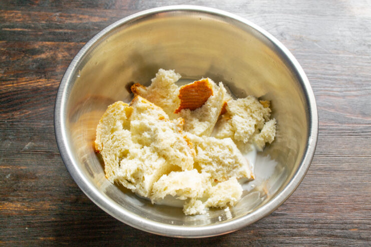 Soaking Stale Bread in Milk for Juicy Sausages A bowl with pieces of stale white bread soaking in milk.