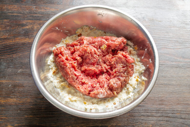 Combining Ground Beef with Soaked Bread Mixture Adding lean ground beef to a bowl with the mashed bread paste.