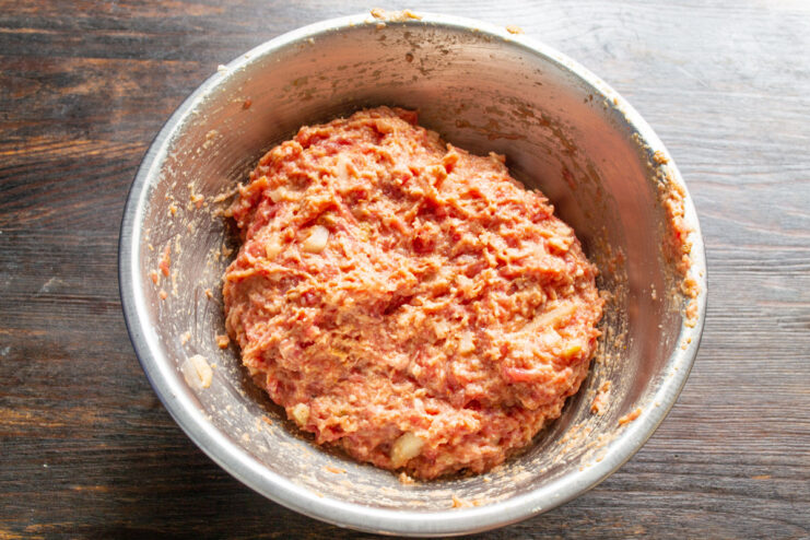 Kneading the Ground Beef Mixture Thoroughly Hands kneading the ground beef mixture in a bowl to combine all ingredients.