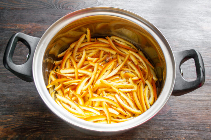 First Boil to Remove Bitterness from Orange Peels A pot of orange peels boiling on the stove, with steam rising.