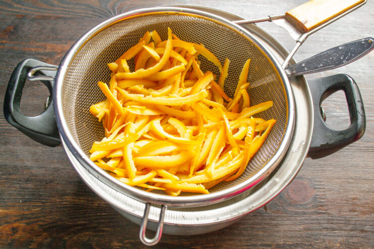 Rinsing the Boiled Orange Peels Boiled orange peels being rinsed under hot water in a colander.