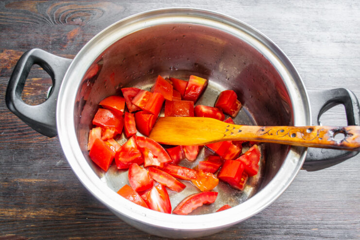 Slicing fresh tomatoes for the Georgian salad. Close-up of hands dicing fresh red tomatoes on a cutting board for the salad.