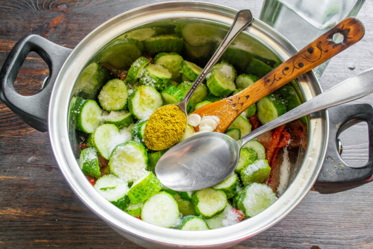 Adding vinegar and khmeli-suneli for authentic Georgian flavor. Pouring vinegar and sprinkling khmeli-suneli spice mix into the pot with the cucumber salad.