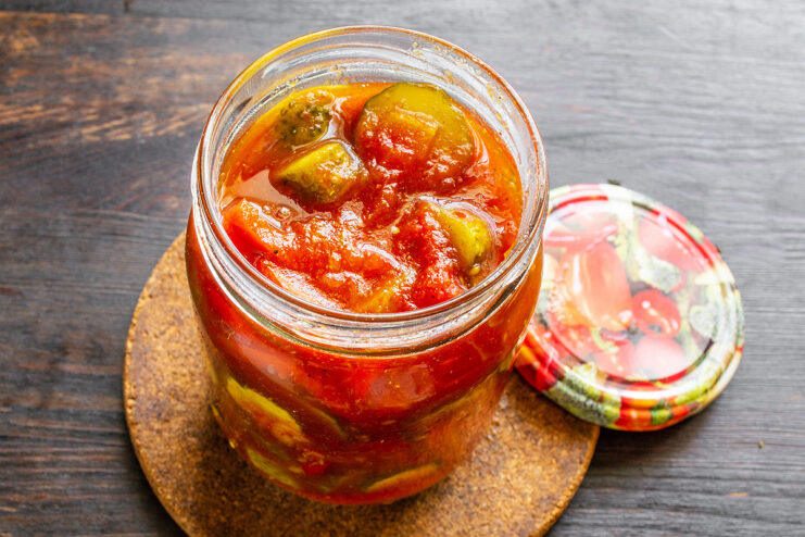 Packing the hot Georgian salad into sterilized jars for canning. Hot Georgian cucumber salad being carefully ladled into a sterilized glass jar.