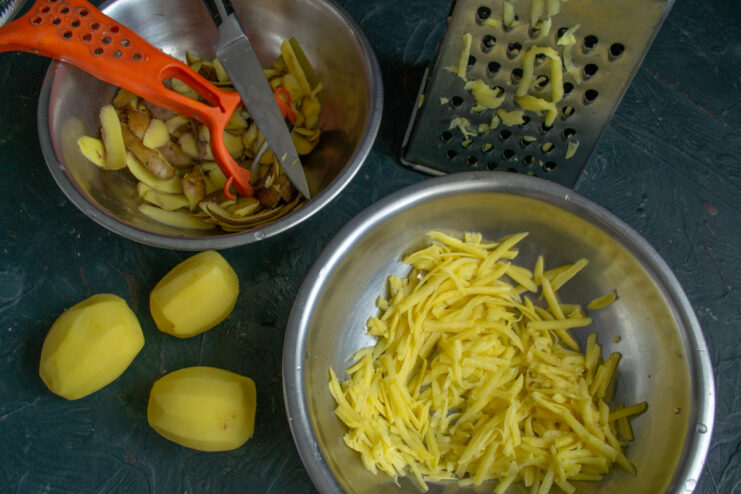 Use a coarse grater for the potatoes to achieve the perfect texture for the draniki. Grating peeled potatoes into a deep bowl using a box grater.
