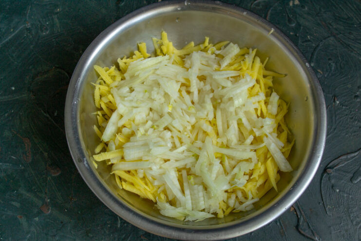 Chopping the onion very finely ensures it cooks evenly within the potato pancake. A hand finely chopping a yellow onion on a cutting board.